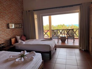 A hotel room with two beds, a brick wall, a balcony with a view, and a large window. - Melon Resort Mũi Né (Phu Thuy)