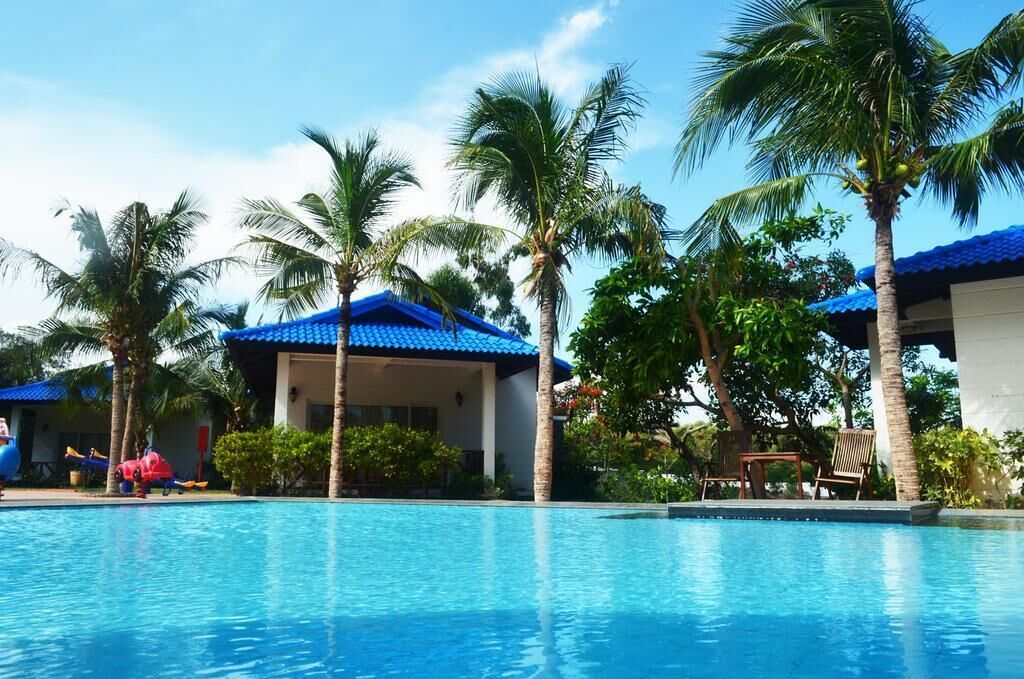 A swimming pool surrounded by palm trees and a building with a blue roof.