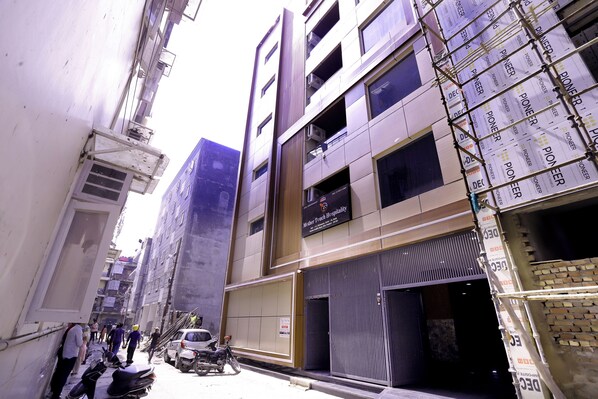 A narrow urban street with buildings, some under construction with scaffolding, and a few parked vehicles.