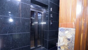 Un ascenseur doté d’un écran numérique, entouré de carreaux de granit foncé.