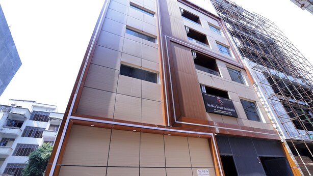 Un immeuble à étages doté d’une façade moderne, comprenant un panneau vertical en bois particulièrement visible et une enseigne pour les hôpitaux Mother Touch.