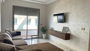 Una sala de estar moderna con un sofá, una mesita de centro, un televisor montado en la pared y una planta en maceta.