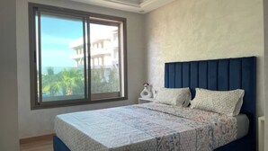 Un dormitorio con un ventanal grande, una cama con ropa de cama estampada y un cabecero azul.