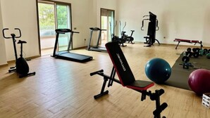 Un gimnasio espacioso con cintas de correr, elípticas, banca y pesas sueltas.