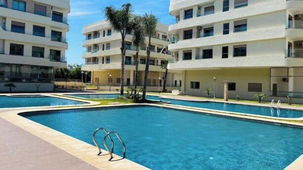 Un hotel moderno con varios pisos, piscina y palmeras.
