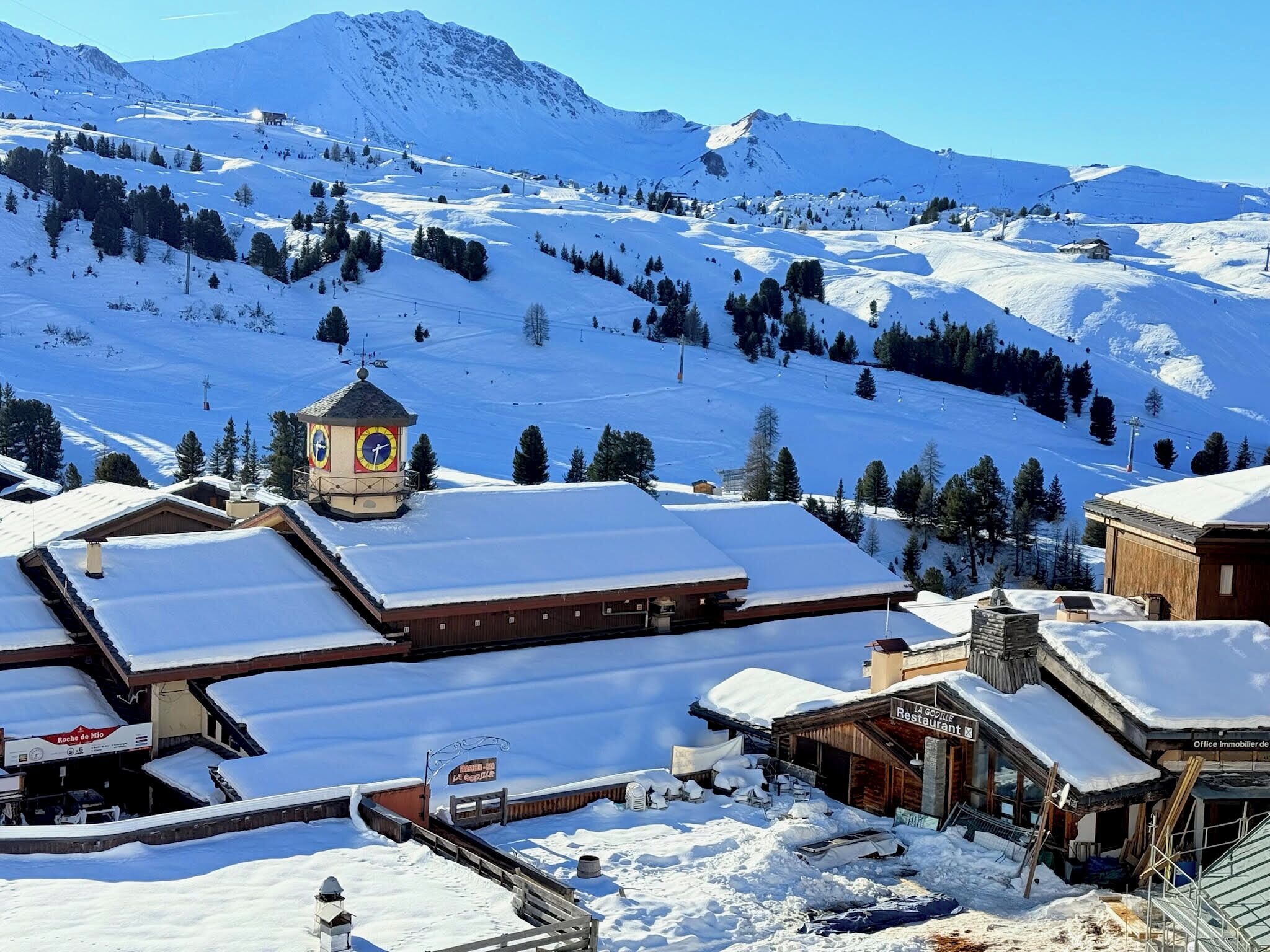 A snow-covered mountain town with a clock tower, wooden buildings, and a ski slope in the background.
