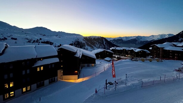 Ein schneebedecktes Bergresort mit mehreren Gebäuden, Skipisten und blauem Himmel.