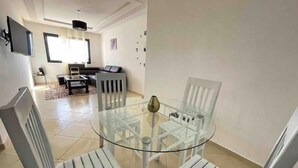 A modern living room with a glass dining table and white chairs, a sofa, and a TV mounted on the wall. - Beautiful, spacious apartment (Témara)