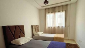 A bedroom with two beds, a window with curtains, and a brown rug. - Beautiful, spacious apartment (Témara)