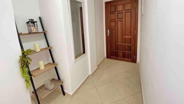A hallway with a wooden door, a white wall, a shelf with candles and a lantern, and a tiled floor. - Beautiful, spacious apartment (Témara)