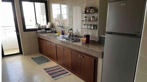 A kitchen with a refrigerator, stove, sink, and storage shelves. - Beautiful, spacious apartment (Témara)