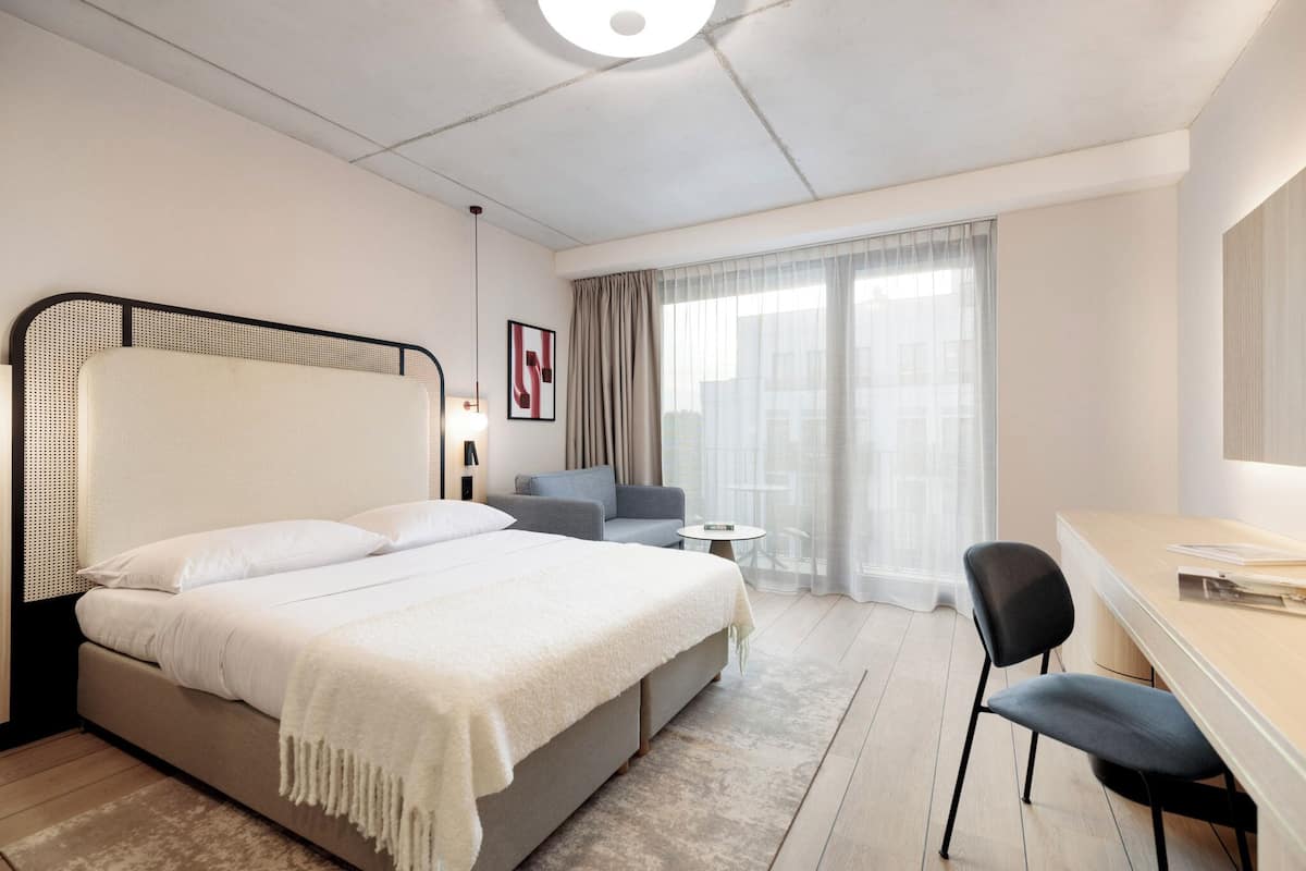 A modern hotel room with a large bed, a desk, a chair, and a small table.