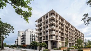 Un edificio de varios pisos con balcones, un sendero pavimentado y abundante vegetación.