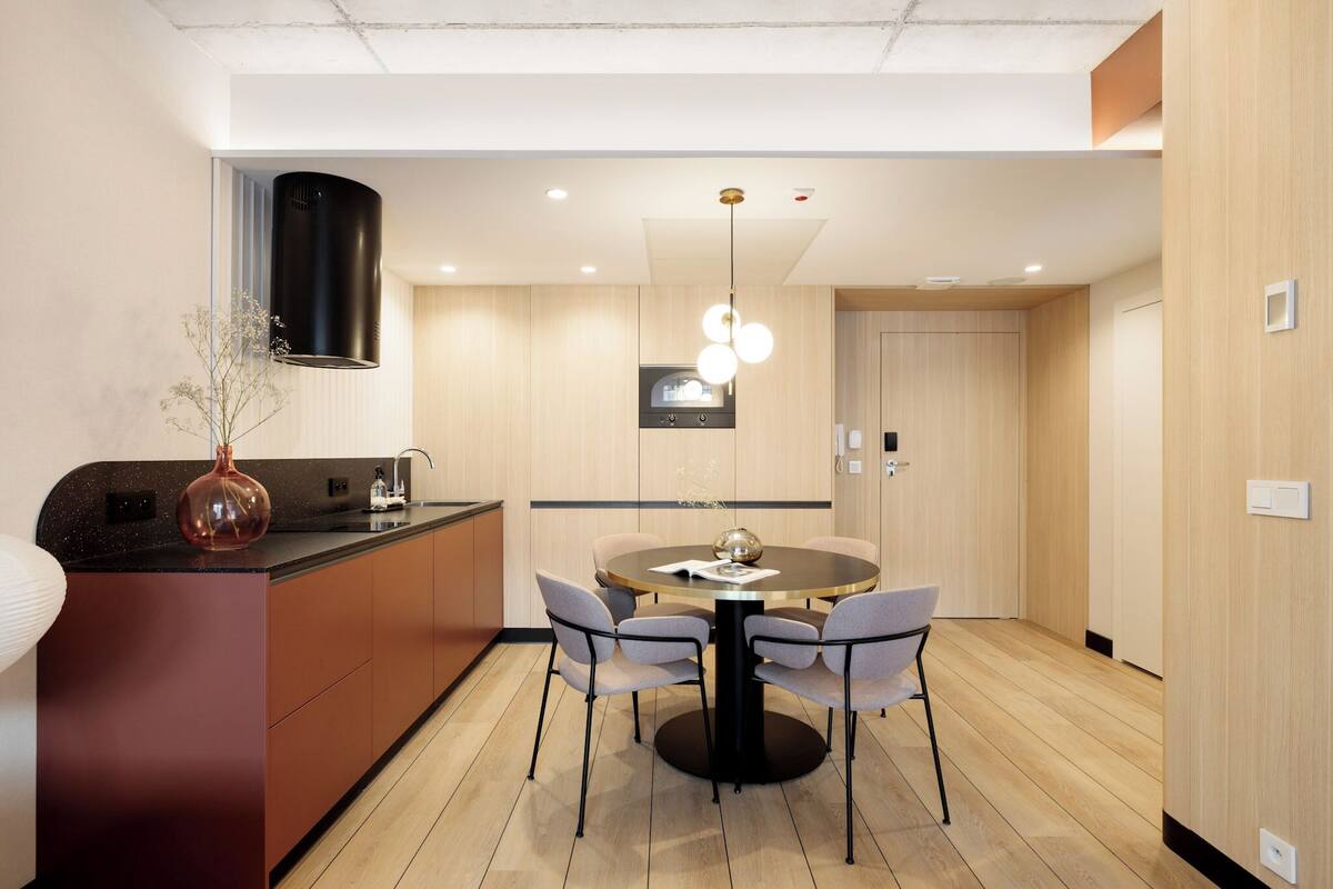 A modern kitchen with a central island, a dining area with a round table and chairs, and a pendant light above the table.