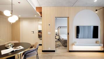 Ein modernes Hotelzimmer mit Essbereich, einem an der Wand montierten Fernseher und einer Wand mit Holzelementen.