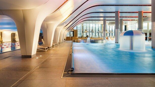 Una amplia piscina interior con un diseño arquitectónico moderno, que presenta techos curvos y ventanas grandes.