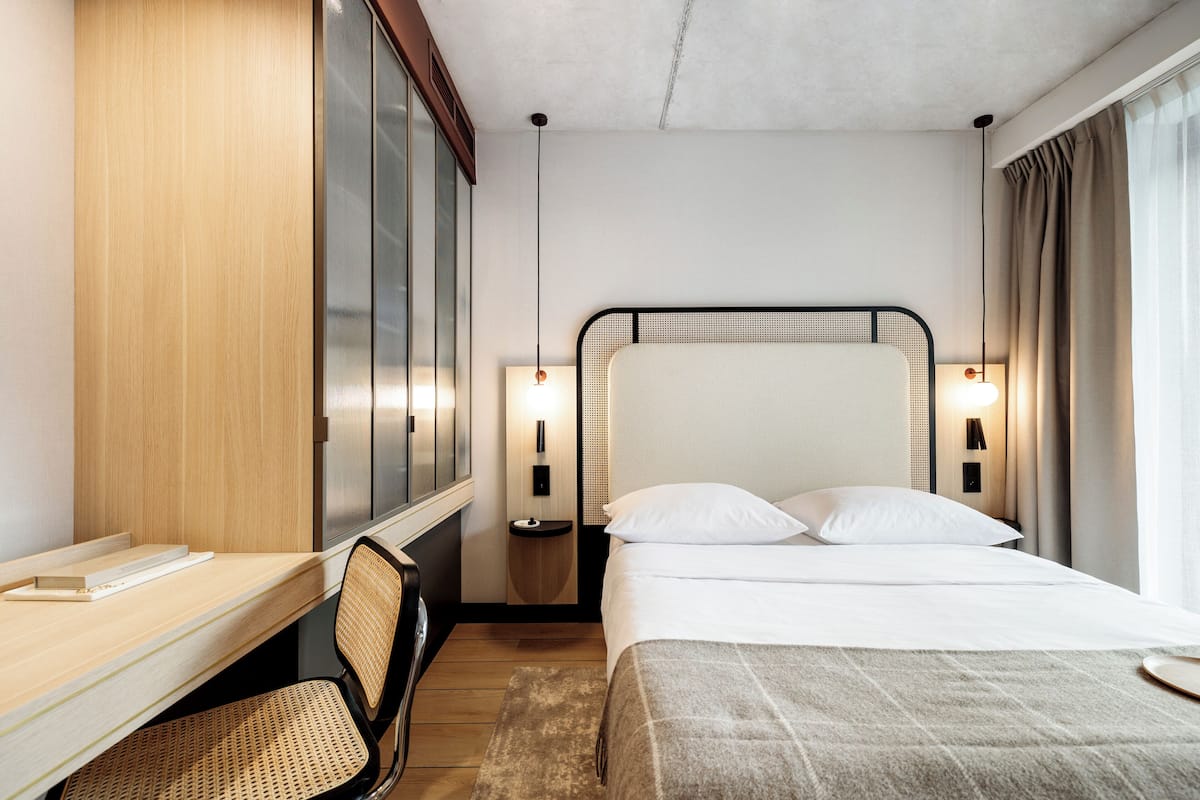 A hotel room with a bed, desk, chair, and bedside lamps.