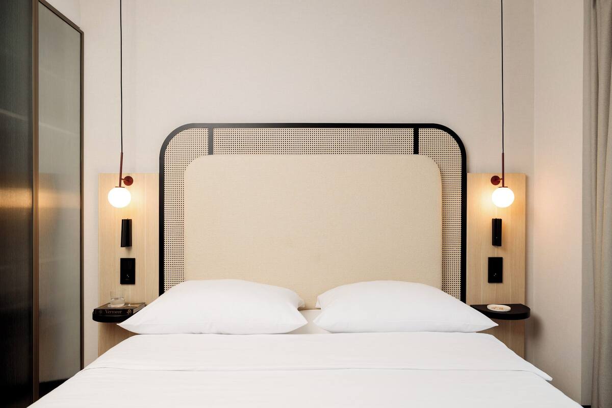 A neatly made bed with white linens and two pillows, a black metal headboard, and two wall-mounted light fixtures on either side.