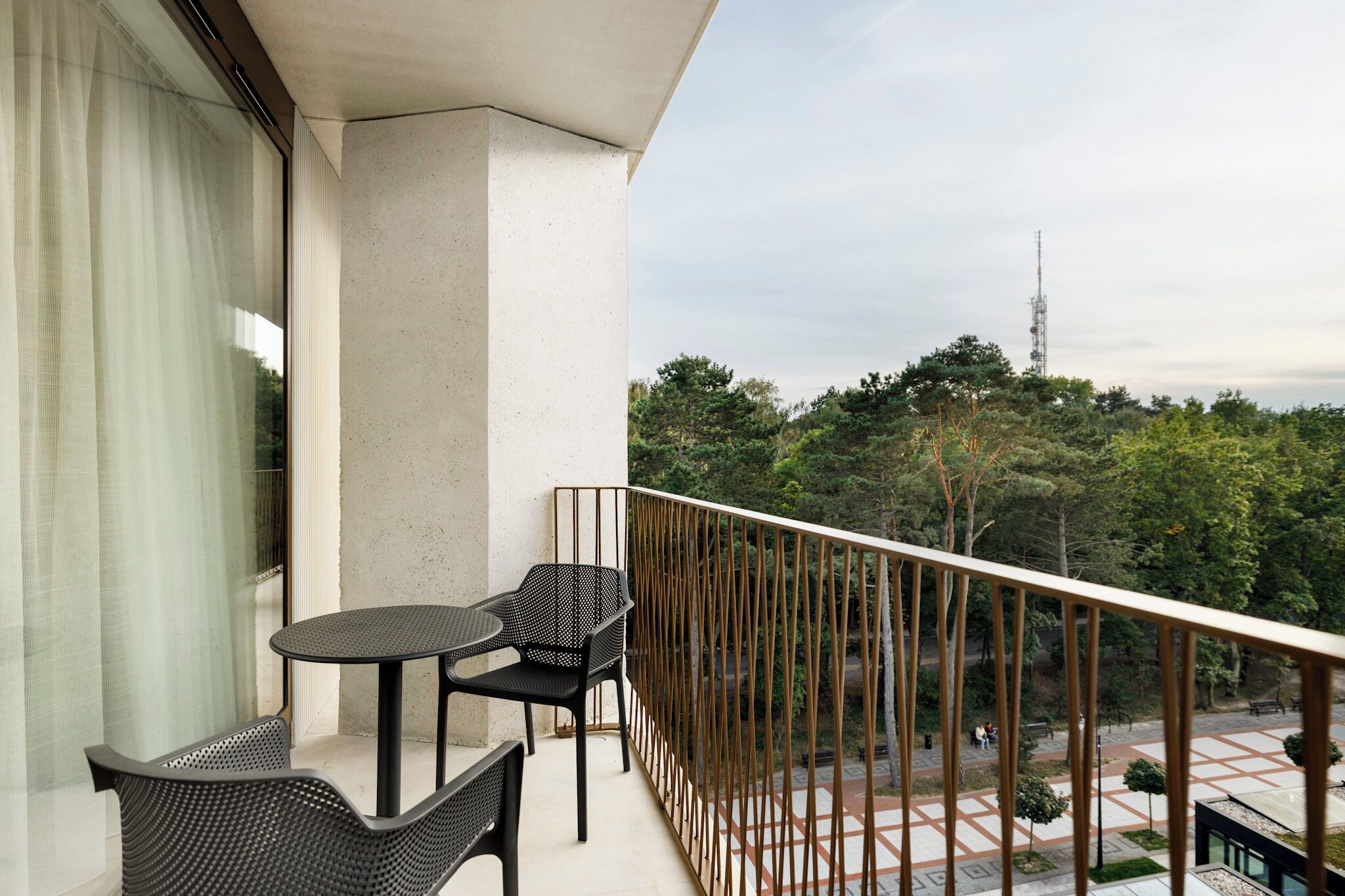 A balcony with a table and chairs, a view of a park, and a tall structure in the distance.