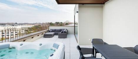 A rooftop terrace with a hot tub, outdoor seating, and a view of the city.