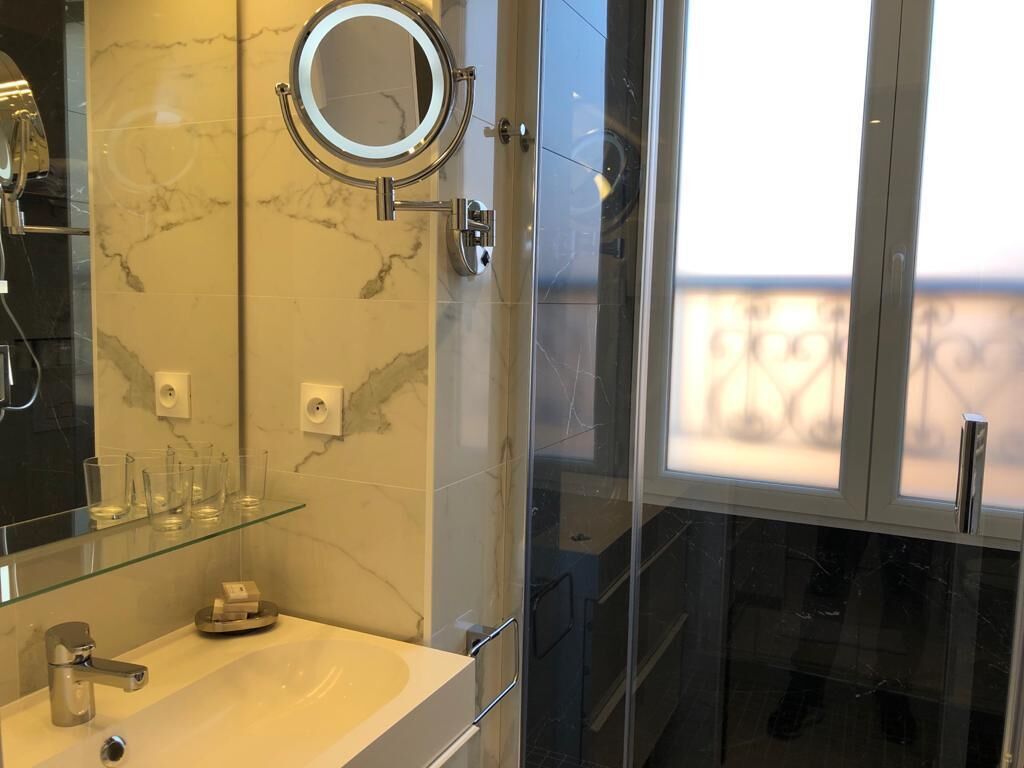 Ein modernes Badezimmer mit Duschkabine aus Glas, einem runden Spiegel und einer Marmor-Spritzschutzwand.