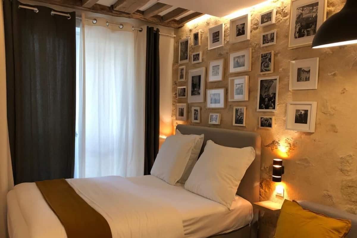 A hotel room with a bed, a bedside table, a lamp, and a wall decorated with framed photos.