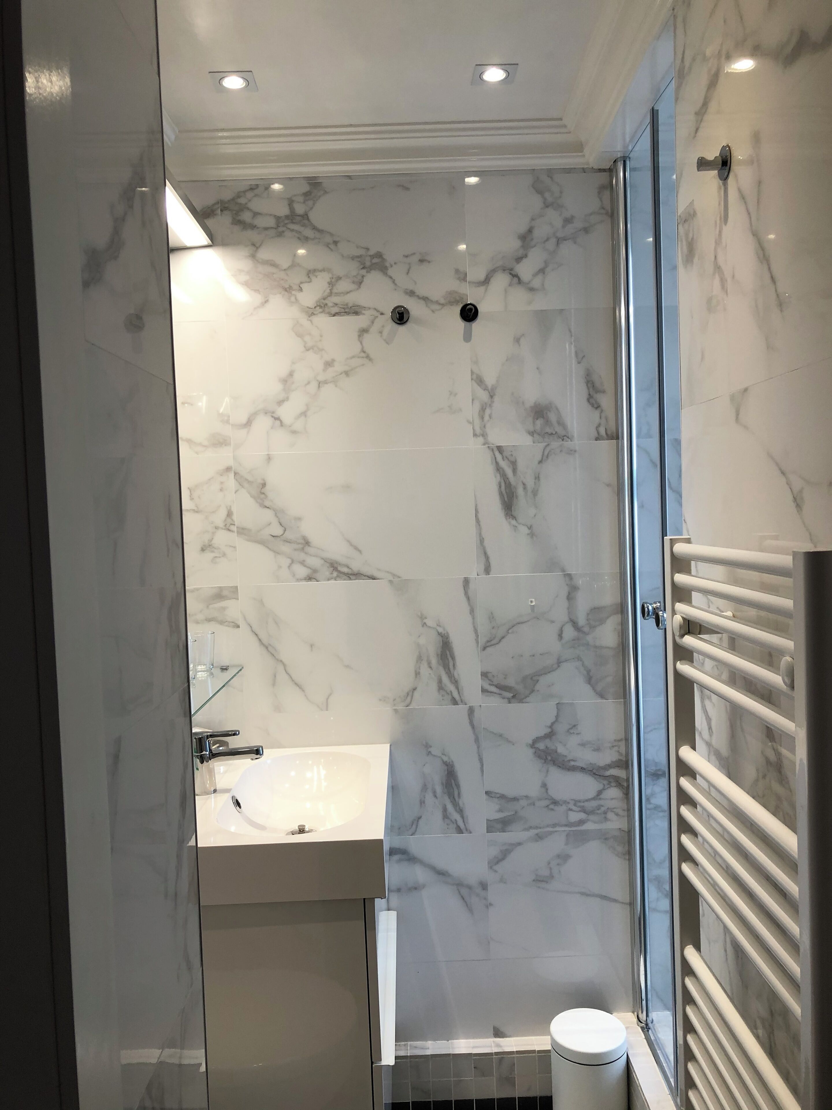 Een moderne badkamer met marmeren wanden, een glazen douchecabine, een witte wastafel en een handdoekhouder.