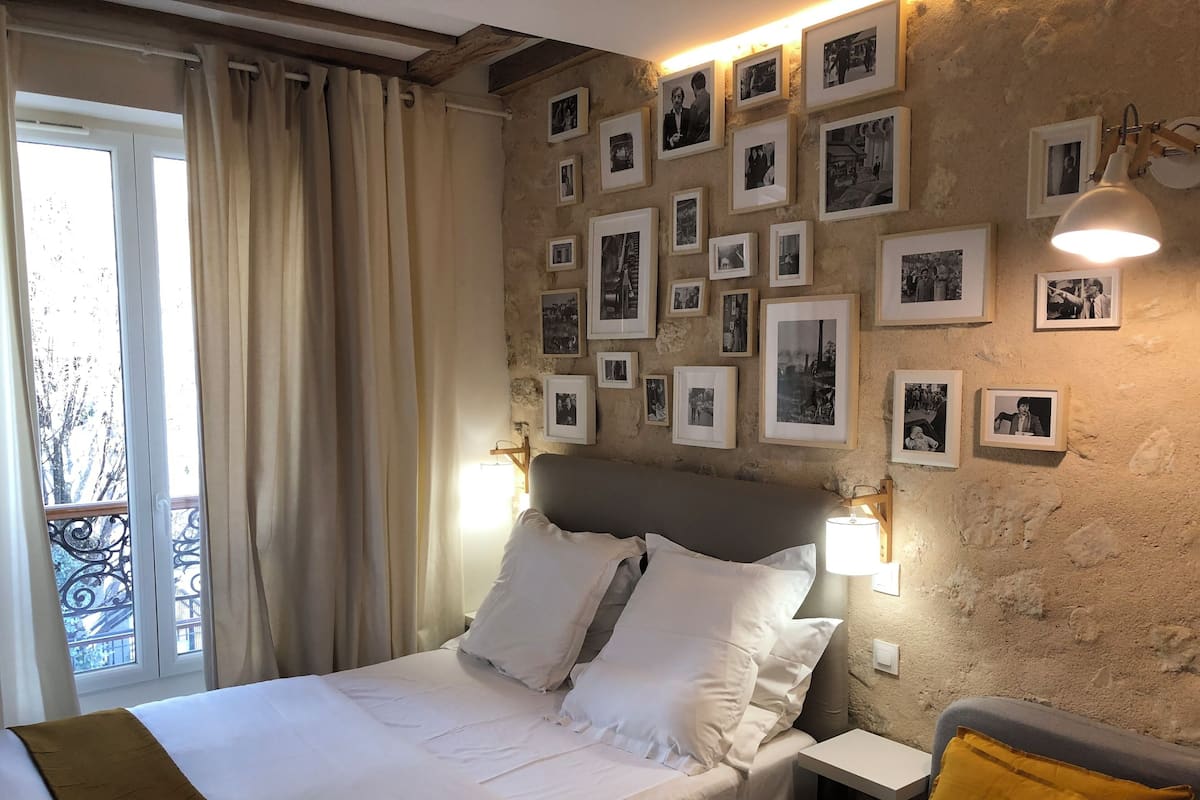 A bedroom with a bed, a nightstand, a lamp, and a wall adorned with framed photographs.