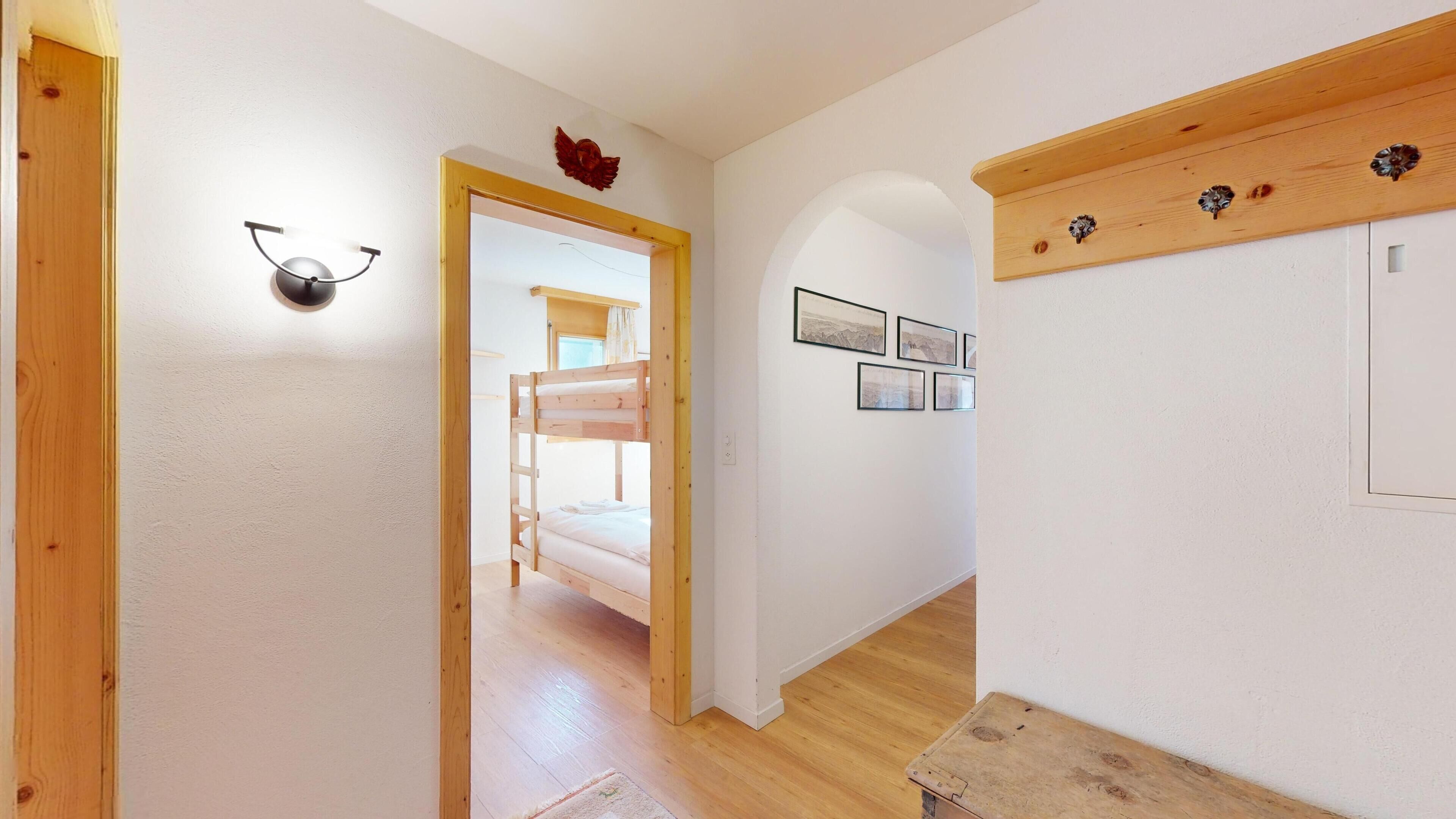 En hall med en våningssäng i trä som syns i bakgrunden, en vägglampa och inramade bilder på väggen.