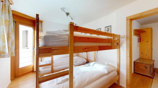 A bunk bed room with wooden frames, white bedding, and a window with curtains.