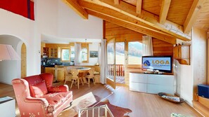 A spacious living area with a red sofa, wooden flooring, a dining table, and a kitchen in the background.