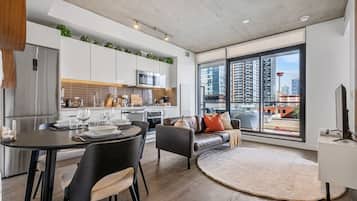A modern apartment with a dining area, kitchen, living room, and large windows offering city views.