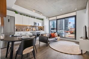 A modern apartment with a dining area, kitchen, living room, and large windows offering city views. - Calgary Tower View | Central DT | Gym (Calgary)