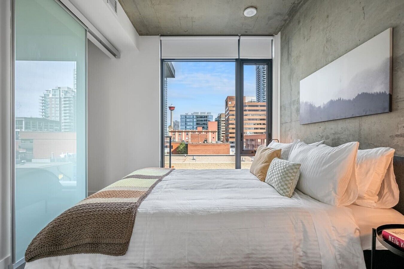 A modern bedroom with a large bed, a view of the city, and a painting on the wall.