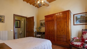 Ein Schlafzimmer mit einem großen Bett, einem Holzschrank, einem Sessel und einem Bild an der Wand.