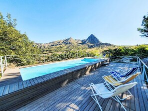 A wooden deck with a swimming pool and lounge chairs overlooking a mountainous landscape.