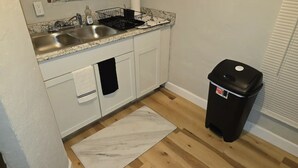 Eine Küche mit weißen Schränken, einer doppelten Spüle, einer schwarzen Mülltonne und einem Teppich mit Marmor-Muster.