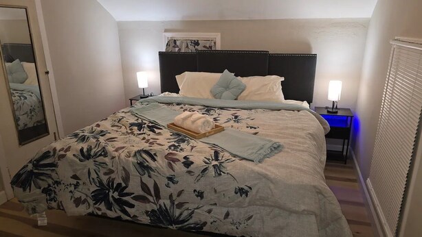 Ein ordentlich bezogenes Bett mit Blumenmuster, zwei Nachttischlampen und ein Nachttisch mit Lampe.