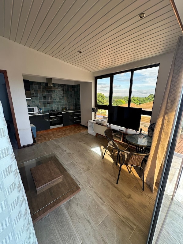 Una cocina moderna con baldosas oscuras, un comedor con mesa de vidrio y un amplio ventanal con vistas a zonas verdes.