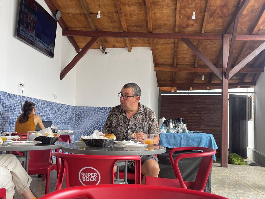 Un restaurante con vigas de madera en el techo, un televisor montado en la pared y sillas rojas y negras.