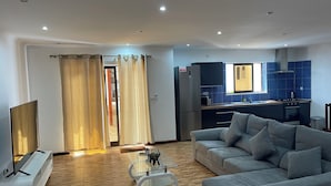 A modern living room with a grey sofa, a glass coffee table, and a TV stand.