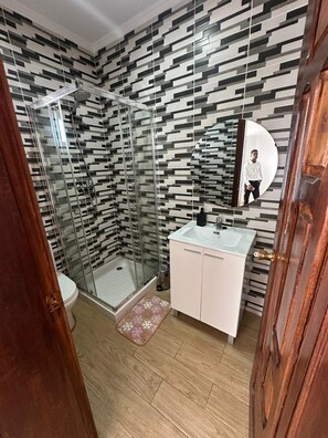 Een moderne badkamer met een douchecabine van glas, een witte wastafel en een behang met een patroon.