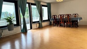 A dining area with a table and chairs, large windows with curtains, a hanging plant, and a ceiling light fixture. - Beautiful house with backyard  (Partille)