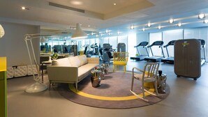 Une chambre d’hôtel moderne avec un canapé, un bureau, une lampe et un tapis de course à l’arrière-plan.