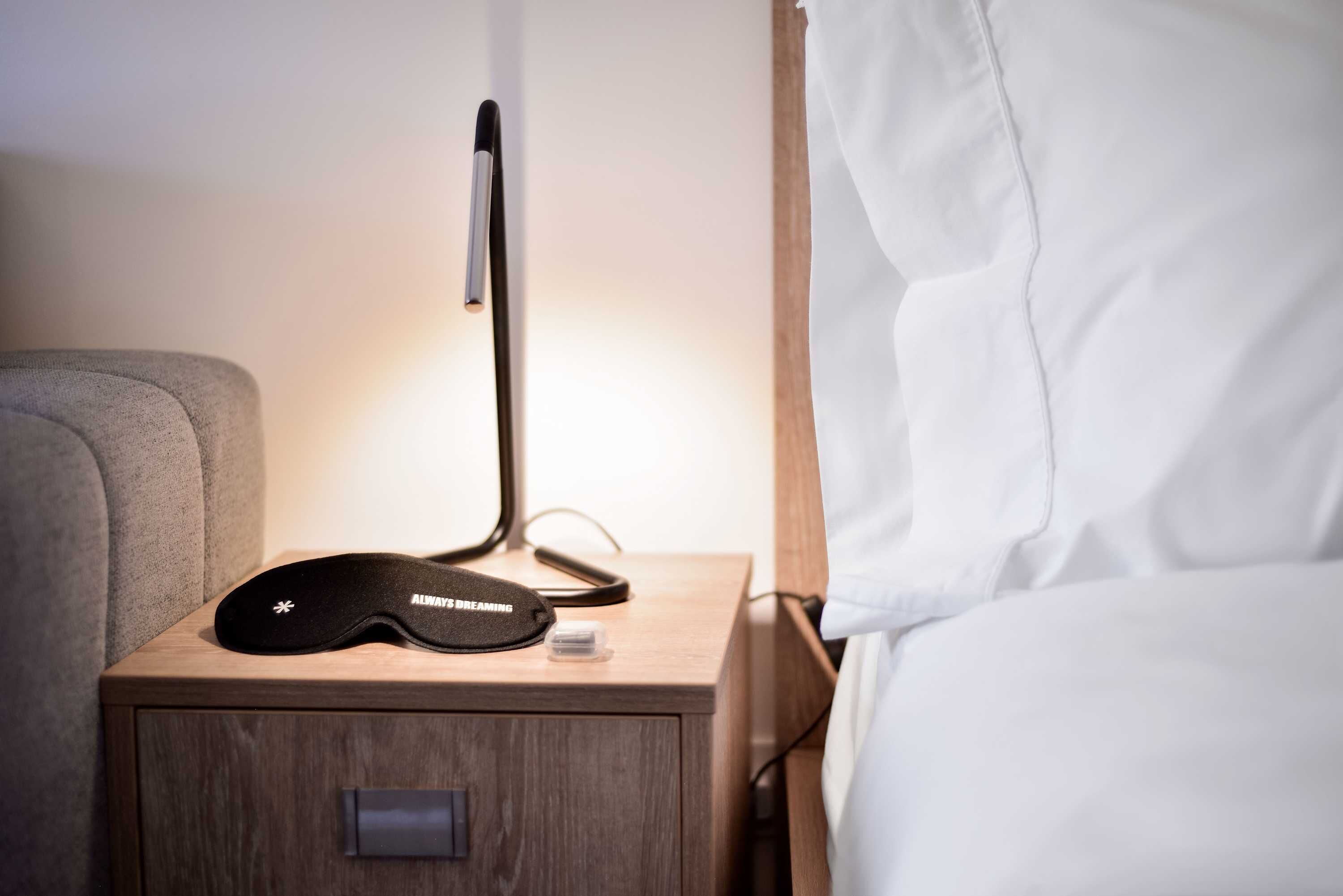 Een nachtkastje met een zwart slaapmasker en een lamp.