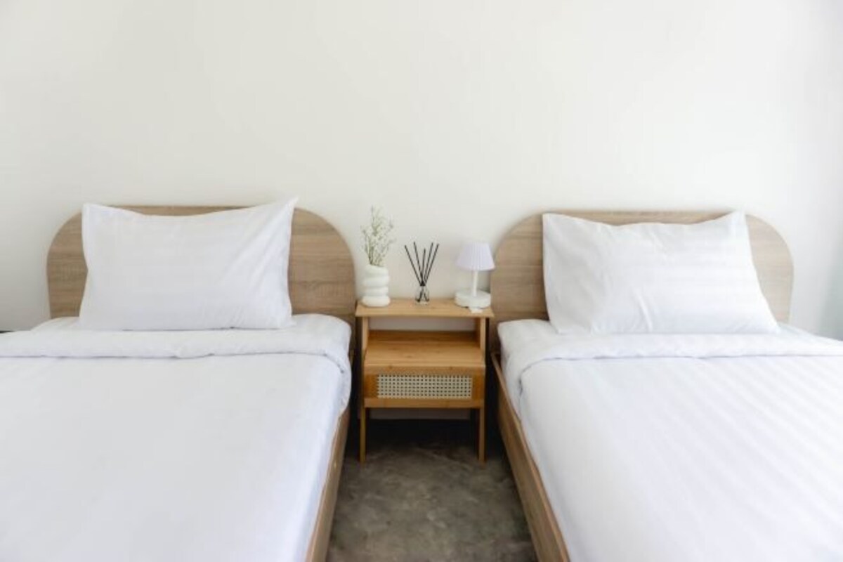 A hotel room with two single beds, a wooden nightstand between them, and a small table with a vase and candles.