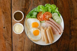 Un plato con huevos, jamón, lechuga, tomates y pepinos sobre una mesa de madera.