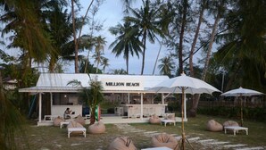 Ein Außenbereich mit Sitzgelegenheiten, wie z.B. Sitzsäcken und Sonnenschirmen, an einem Strandcafé namens 'Million Beach'.