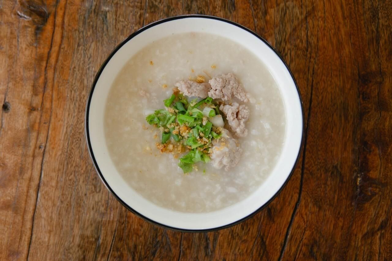A bowl of congee with meat and green onions on a wooden table.