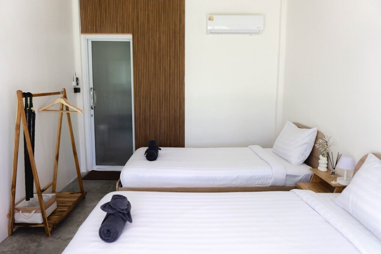 Habitación de hotel con dos camas, un armario de madera, un perchero y una pequeña mesa con una lámpara y adornos.